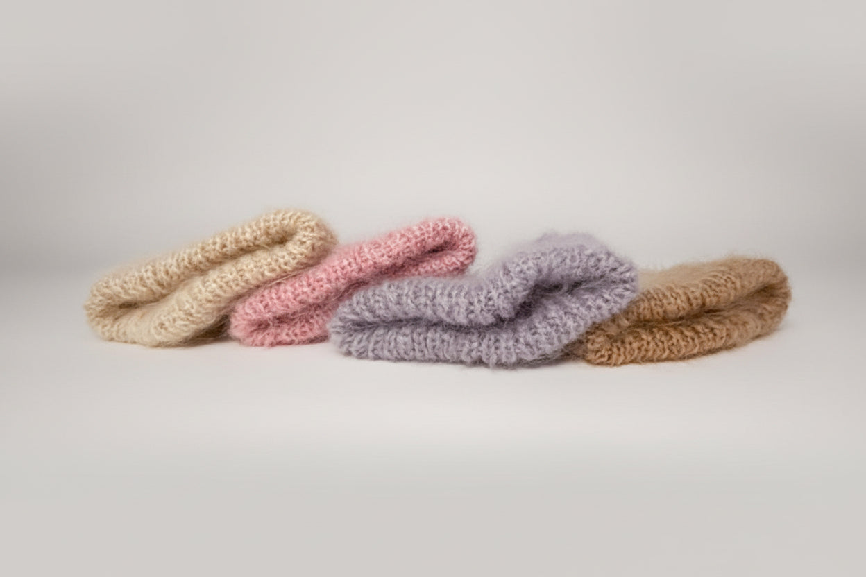 Four knitted scrunchies in beige, pink, purple, and brown on a light gray background