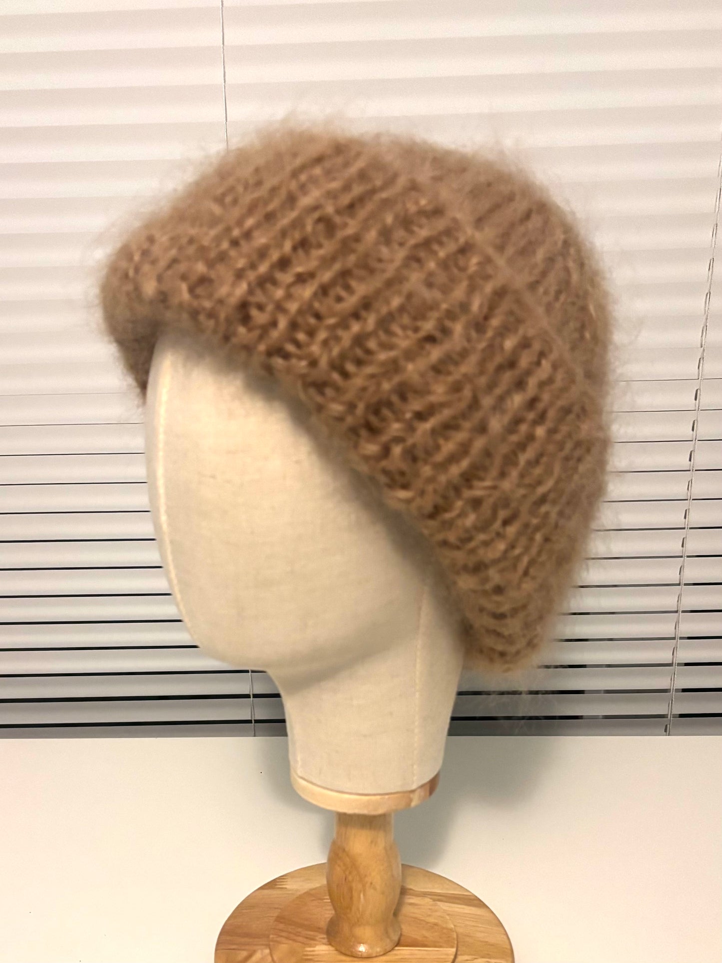 Brown knitted beanie on a mannequin head against a window blind background