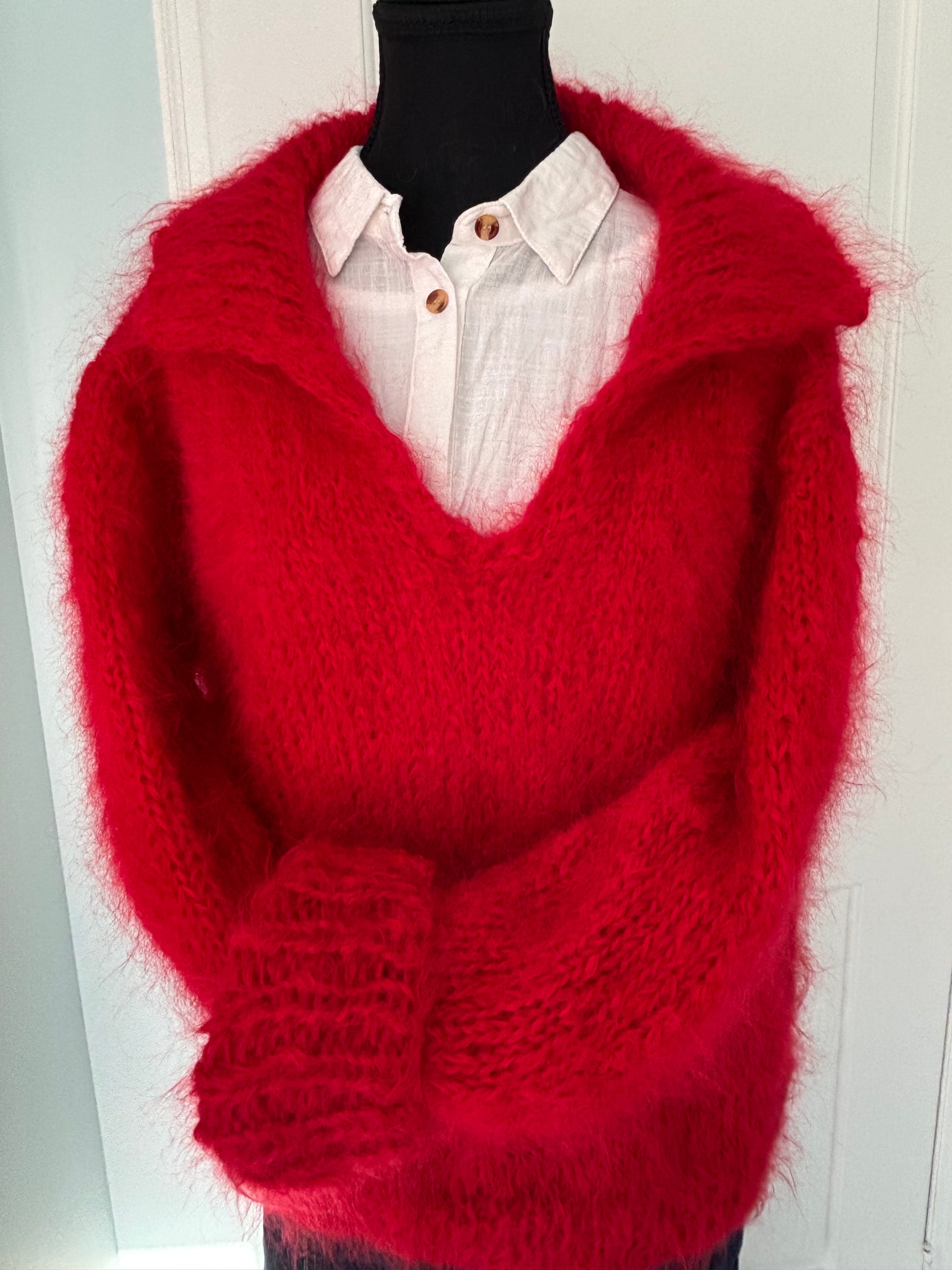 Red knitted sweater draped over a white surface with a blurred background