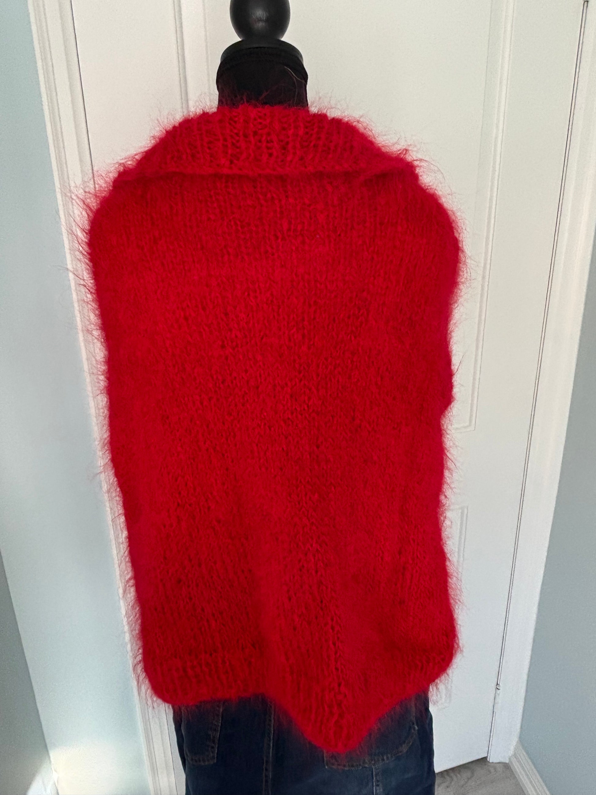 Red knitted hot water bottle cover on a white cabinet.