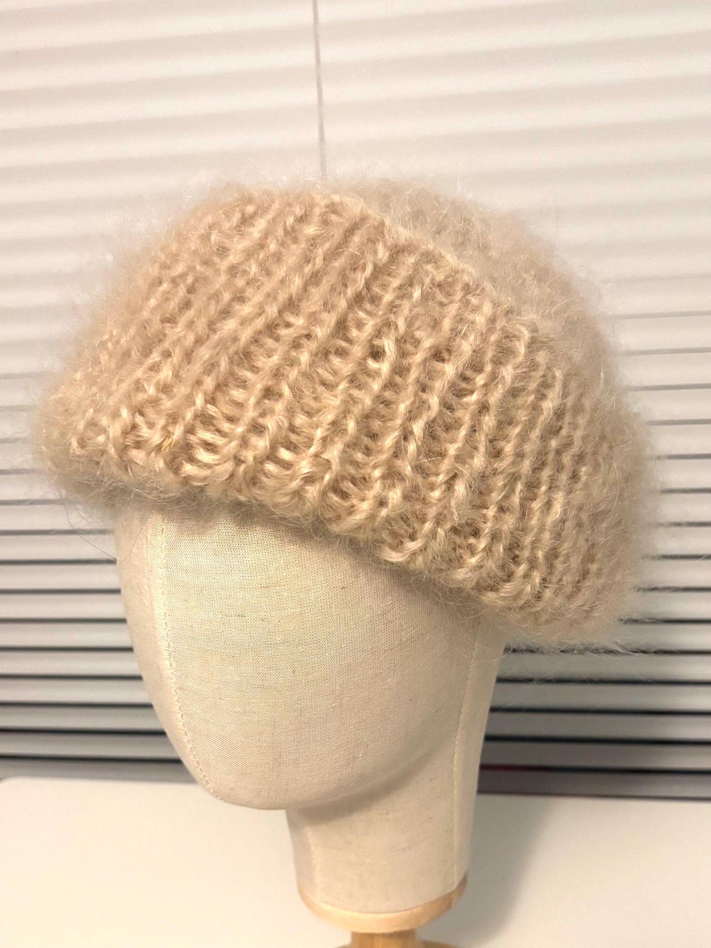 Beige knitted hat on a mannequin head against a white background