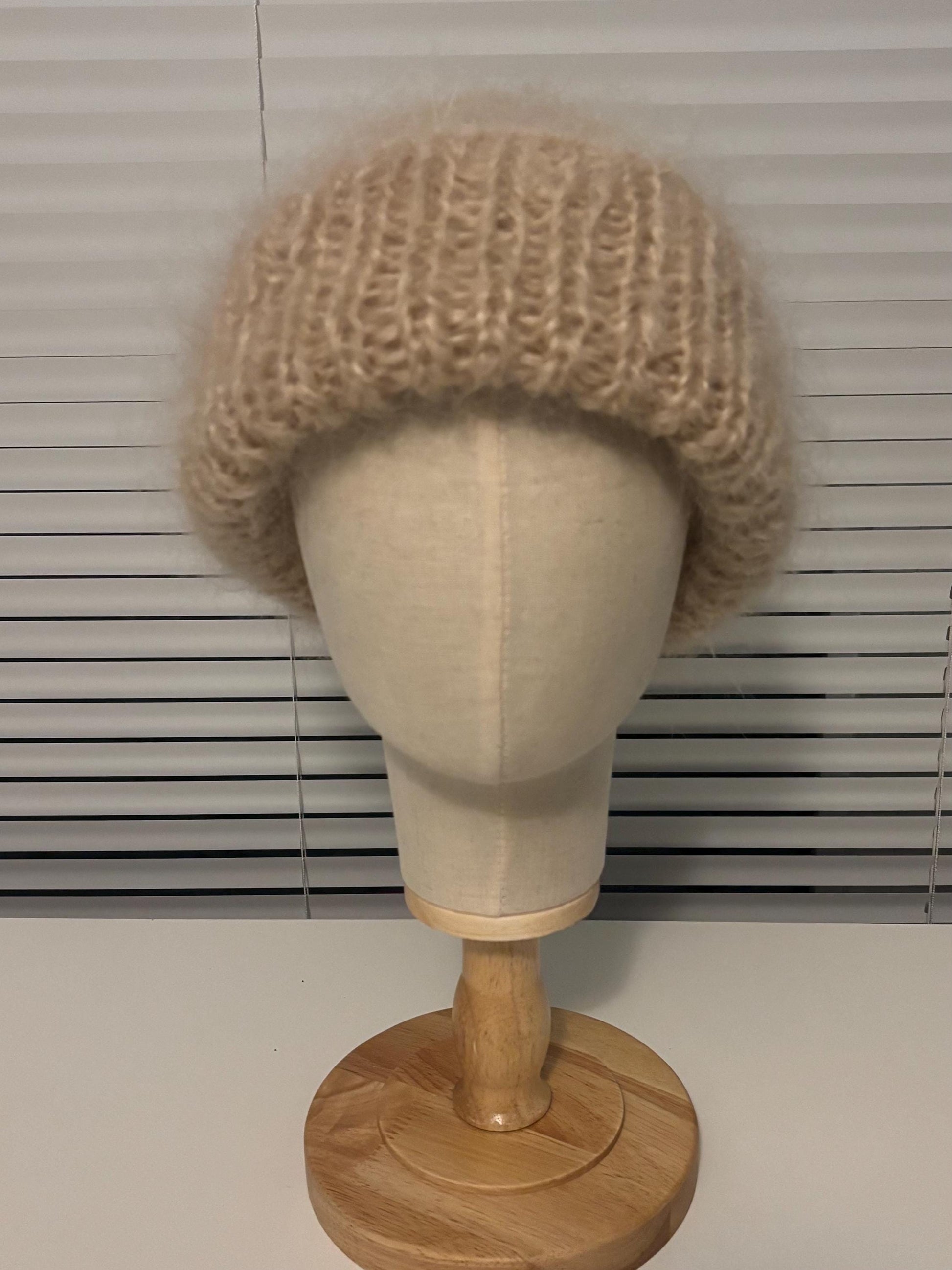 Beige knitted hat on a mannequin head against a window blind background
